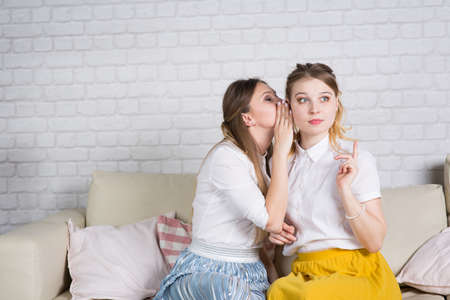 Two young girls are sitting on the couch, a friend at a party