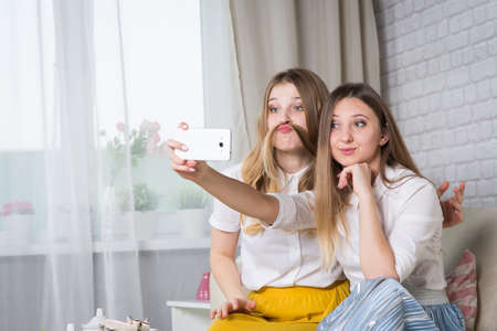 Two young girls are sitting on the couch and making selfi, a friend at a party