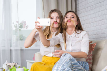 Two young girls are sitting on the couch and making selfi, a friend at a partyの写真素材
