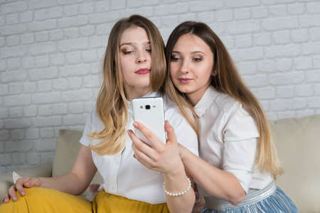 Two young girls are sitting on the couch, a friend at a party