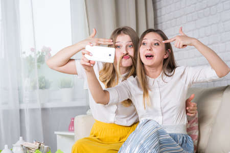 Two young girls are sitting on the couch and making selfi, a friend at a party の写真素材