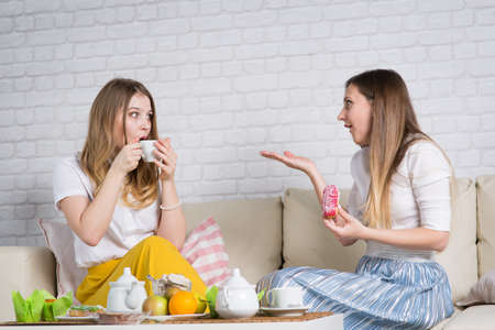 Two young girls are sitting on the couch, a friend at a party 