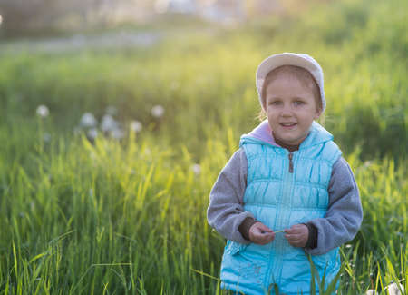 The girl is three years old, walking along the spring clearing with flowersの写真素材