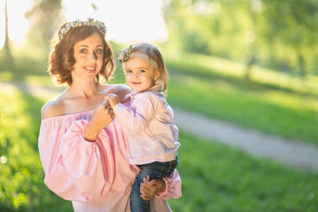 Mom and daughter are two years old sitting on the grass in the park, woman and child in natureの写真素材