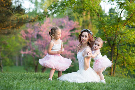 Mom and daughter are two years old and four years old sitting on the grass in the park, a woman and children in natureの写真素材