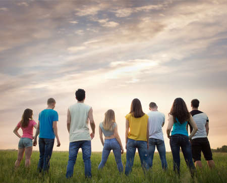 Group  young people, outdoors. People stand with their backs against the beautiful sunset skyの写真素材