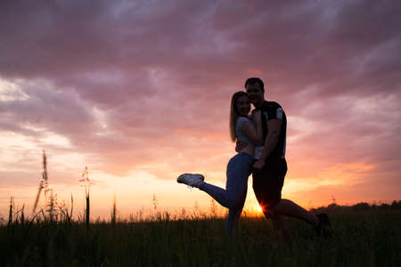 Silhouette of a young couple stand with their backs on a beautiful sunset sky