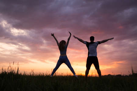 Silhouette of a young couple jumping against the beautiful sunset skyの写真素材