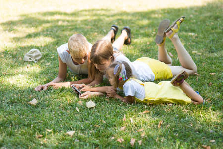 company of three children in the park are sitting on the grass with a phoneの写真素材