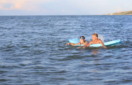 Two children on an inflatable mattress bathe in the sea