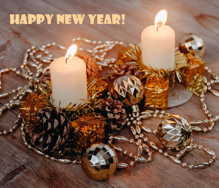 Lighted candles in candle holders with pine cones, tinsel, decorative toy balls and garland on wooden background in dark colors. Merry Christmas Greeting Card wallpaper. New Year winter decor concept.の写真素材