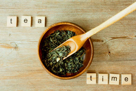Tea time inscription, Chinese, Japanese green dried tea leaves at bamboo scoop and round bowl close...