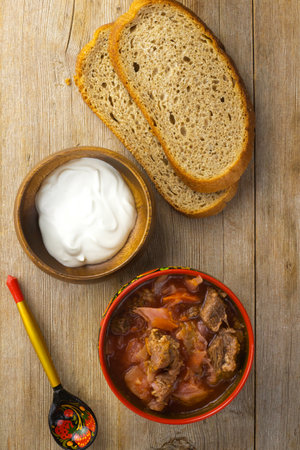 Borscht russian ukrainian traditional vegetable cabbage beetroot soup in red bowl with khokhloma pattern on natural wooden table background flat lay, top view. Close up. Selective focus. Copy spaceの写真素材
