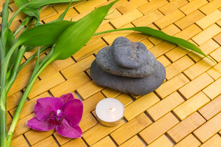 Spa, zen, massage concept. Bamboo leaves, black stones, purple orchid, candle on wood backgroundの写真素材