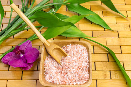 Spa, zen, massage concept. Pink himalayan bath salt with spoon, bamboo leaves, orchid, soap dishの写真素材