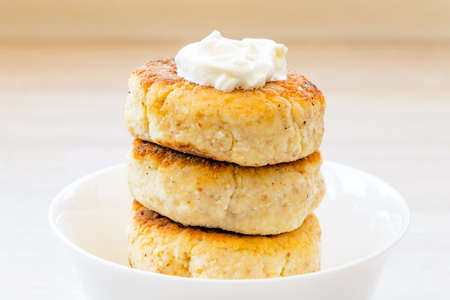 Homemade cottage cheese pancakes syrniki stack on round glossy white bowl on white rustic natural wooden table background. Close up. Selective focus. Copy spaceの写真素材
