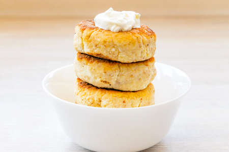 Homemade cottage cheese pancakes syrniki stack on round white bowl on white rustic table backgroundの写真素材