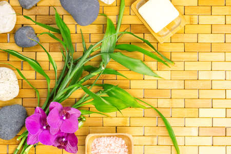 Spa, zen, massage concept. Bath salt, bamboo leaves, soap in soap dish, white black stones, purple orchid on wooden background. Top view. Flat lay. Close up. Selective focus. Copy space.の写真素材