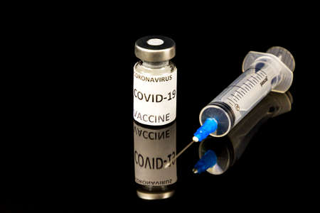 Glass vial Vaccine label Covid - 19 Coronavirus Vaccine text and medical syringe isolated on black...