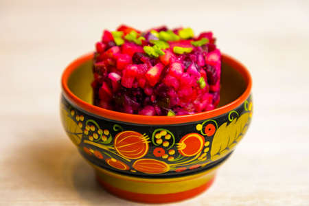 Vinegret Russian beet salad of boiled vegetables in painted wooden bowl on white table background. Close up. Selective focus. Copy spaceの写真素材