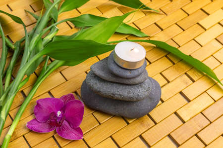 Spa, zen, massage concept. Bamboo leaves, black stones, purple orchid, lighting candle on wooden background. Above view. Close up. Selective focus with copy spaceの写真素材