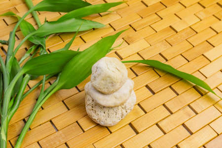 Spa, zen, massage, relaxation concept. Young green bamboo branches, leaves and white stone pyramid on wooden background. Top view. Flat lay. Close up. Selective focus. Copy space.の写真素材