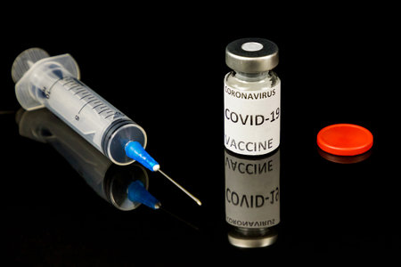 Vaccine bottle withred cap and label Vaccine, medical syringe isolated on black glossy background. Vaccination concept. Close up. Selective focus. Copy spaceの写真素材