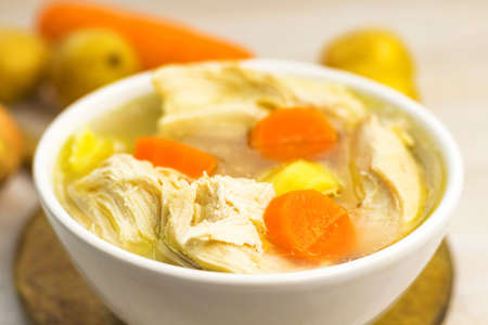 Chicken Soup stew broth and vegetables in white bowl on old rustic wooden cutting board. Close up. Selective focus. Copy spaceの写真素材