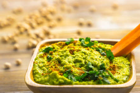 Homemade chickpea hummus with herbs in square bamboo wooden bowl, carrot stickの写真素材