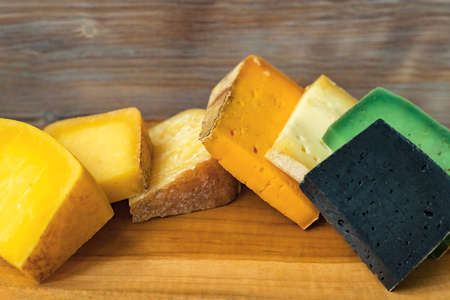 Wooden cutting board with different cheese color chunks on wood wall backgroundの写真素材