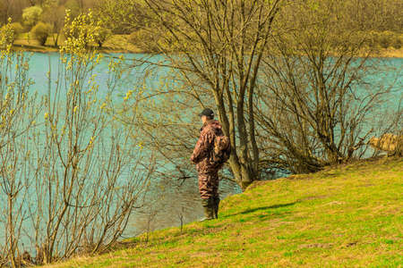 Mature fisherman standing back angling holding fishing rod in hands on pond spring natural bakgroundの写真素材