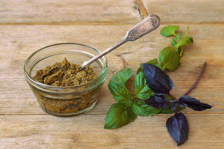 Basil pesto in glass bowl with metal spoon and green purple leaves on wooden table background aboveの写真素材