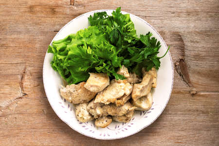 Chicken cream stew with green salad on white plate on wooden table background. Top view. Close upの写真素材