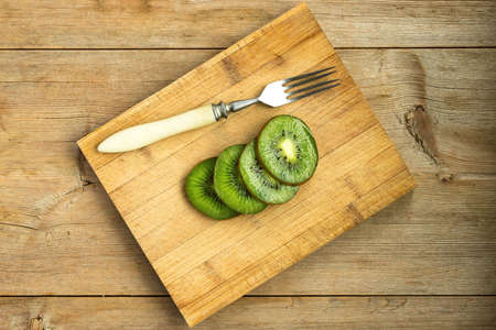 Slices of kiwi fruit on wooden cutting board on wood table with forkの写真素材