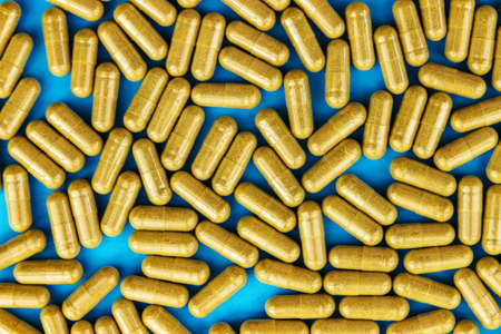 Khaki yellow pills capsules on blue paper background. Full frame medicinal concept. Top view. Flat layの写真素材