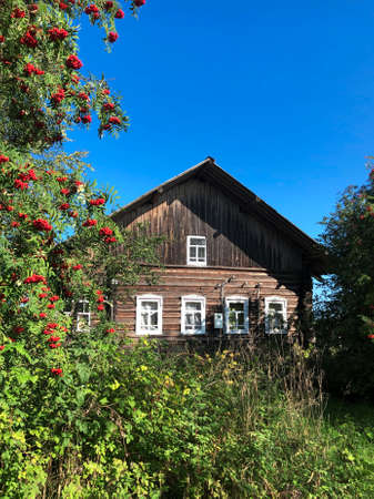 Front of old brown village wooden house with white windows on autumn nature landscape backgroundの写真素材