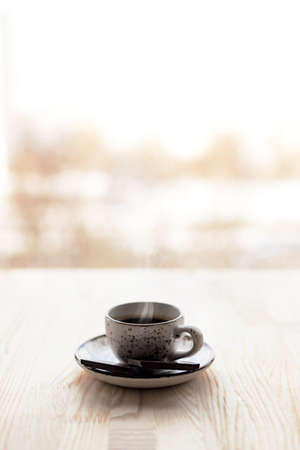 Cup of coffee espresso on saucer on wooden table near window blurred city background.の写真素材