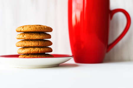 Stack of oatmeal cookie on red plate with coffee cup on white wooden table against wall backgroundの写真素材