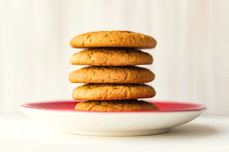 Stack oatmeal cookies on red plate on white wooden table on light wall backgroundの写真素材