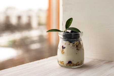 Oatmeal muesli granola with yogurt, blueberry parfait, overnight oats in glass jar on white tableの写真素材