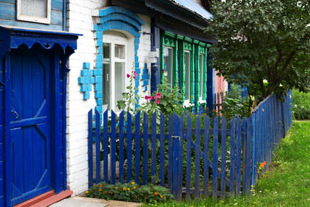 Old wooden and white brick house with green carved window frames, blue door and front garden fenceの写真素材