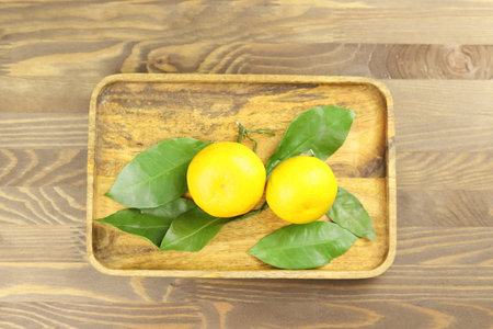 Yellow whole mandarins or tangerine fruits on green leaves on wooden tray. Close-up.の写真素材