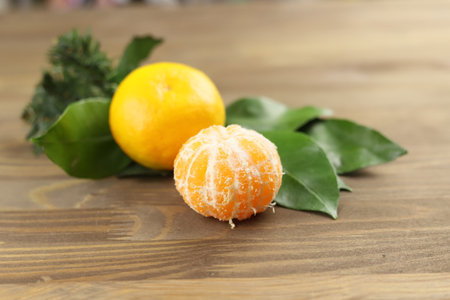 Yellow mandarin or tangerine fruits whole and pilled, green leaves on wooden background, fir treeの写真素材
