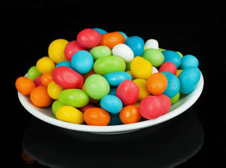 colored candies in white saucer isolated on black background