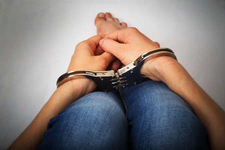 Female hands in handcuffs on a gray backgroundの写真素材