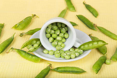 Fresh green peas in an inverted white cup on yellow backgroundの写真素材