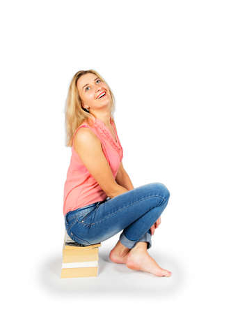 Young woman sitting on a pile of books isolated on white backgroundの写真素材