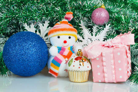 Snowman with blue ball, pink gift box and white snowflake on a background of green garlandの写真素材