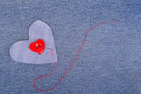 Red heart shaped button with needle and red thread on denim fabricの写真素材