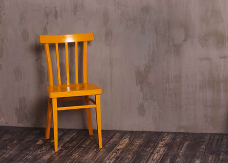 Yellow wooden chair in nterior room with gray decorative plaster wall and dark wooden floorの写真素材